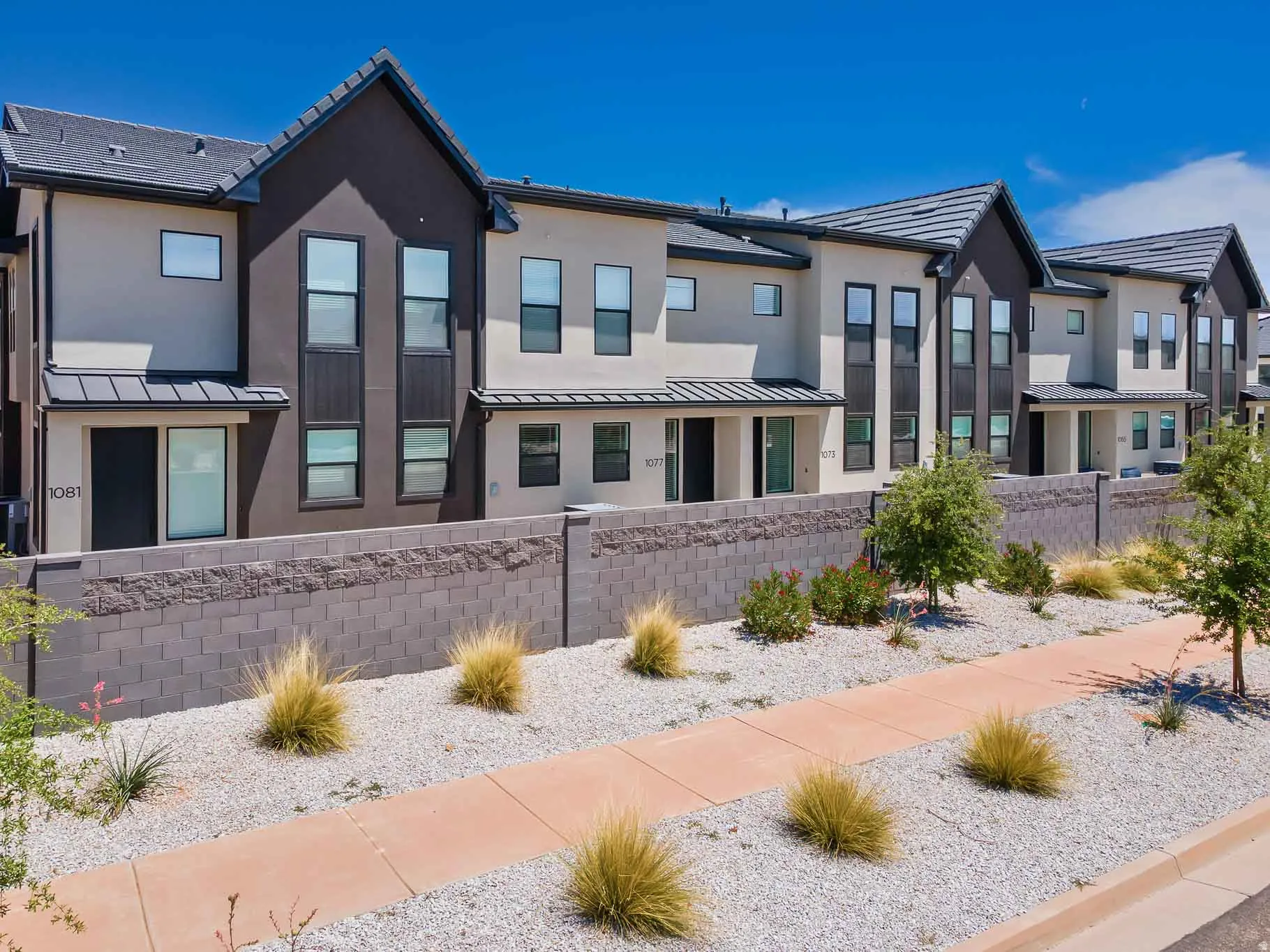 Modern townhome exteriors featuring contrasting stucco and dark siding, a gabled roofline, and contemporary windows