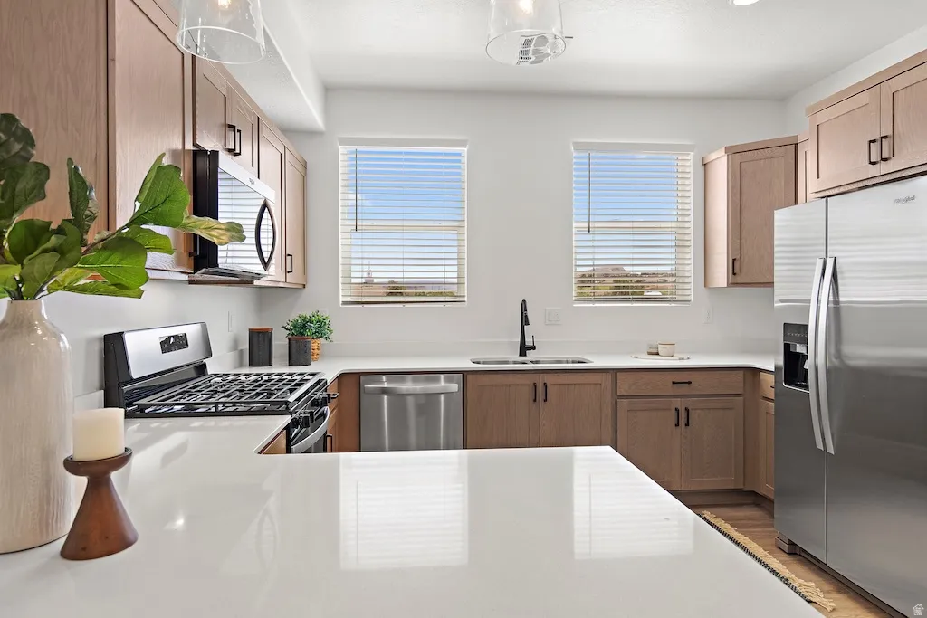 Modern kitchen featuring wood-finish cabinetry, stainless steel appliances, white countertops, and dual windows with blinds