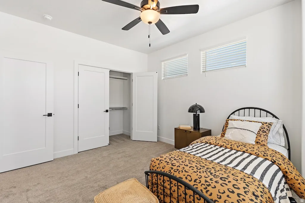 Spacious room featuring neutral carpet flooring, a ceiling fan with integrated lighting, two windows with blinds, and white doors with matte black hardware