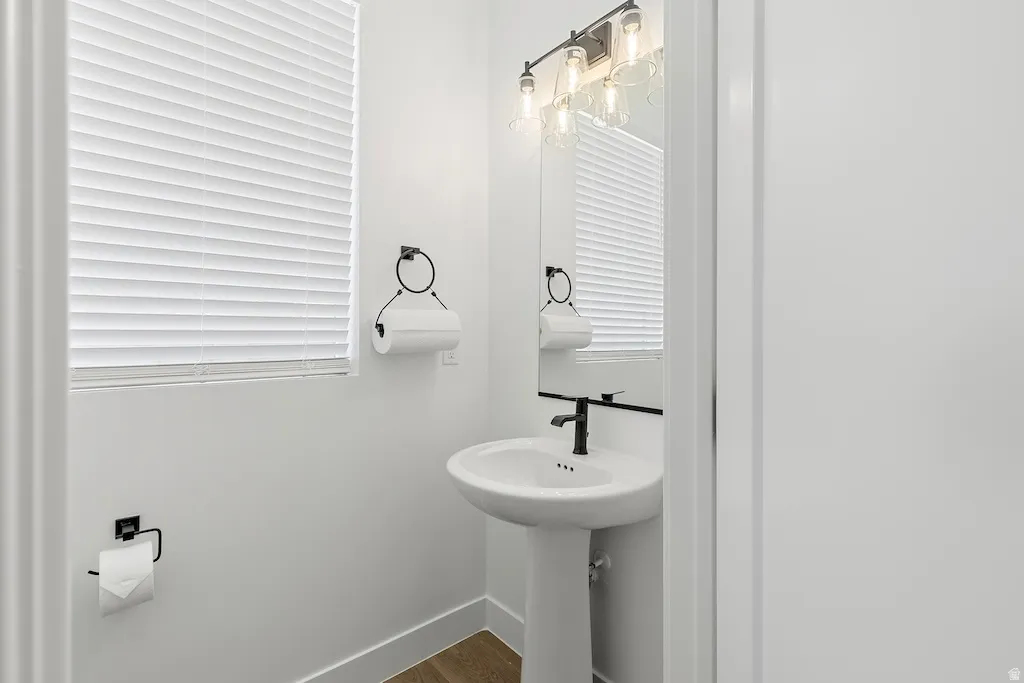 Pedestal sink with a matte black faucet, wall-mounted mirror, and industrial-style vanity lighting