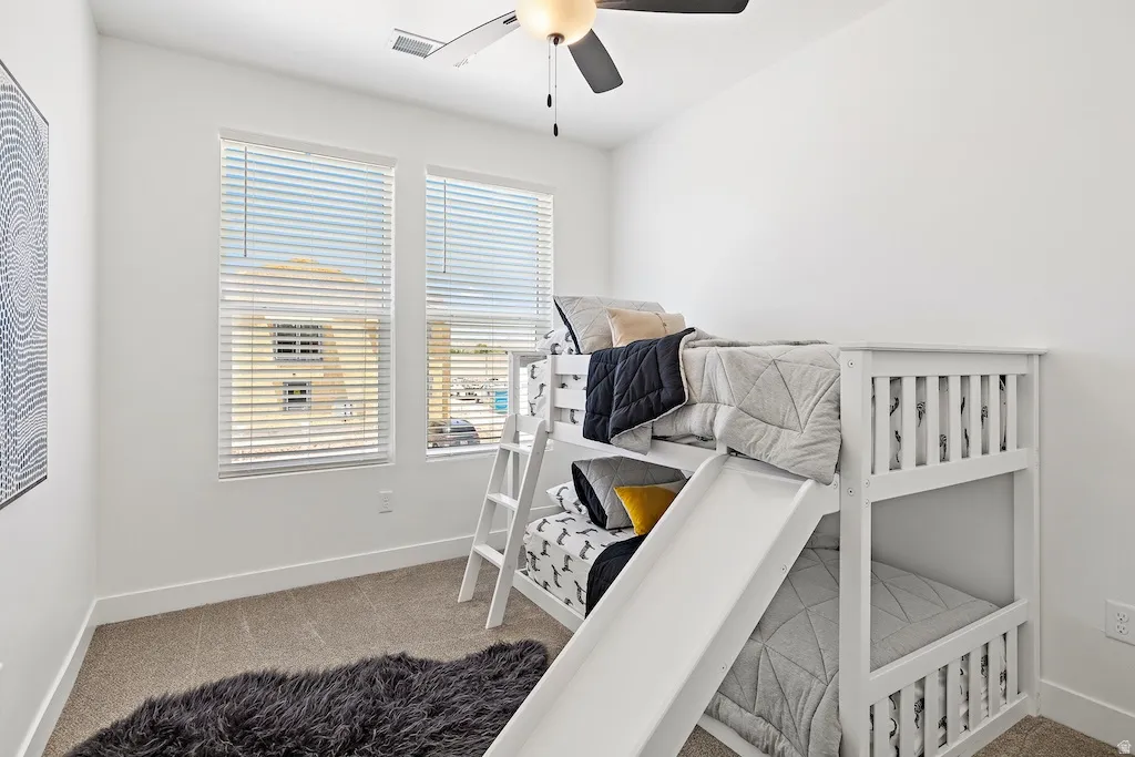 Bright room featuring two windows with blinds, neutral carpeting, and a ceiling fan with integrated lighting