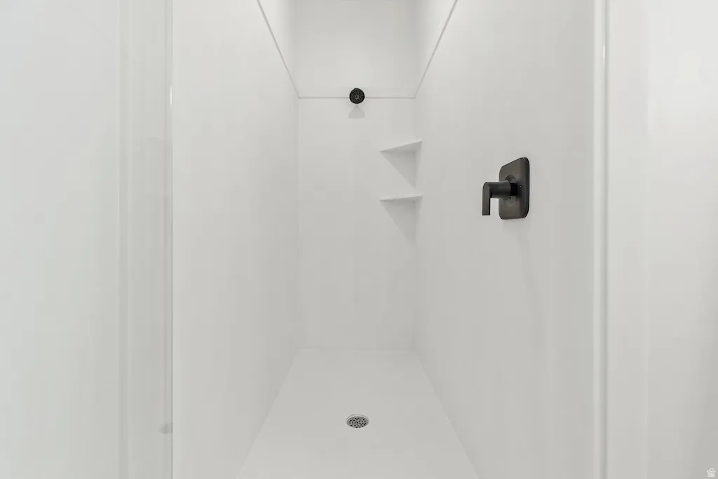 White shower enclosure with dark bronze fixtures, featuring a square shower head and integrated corner shelving