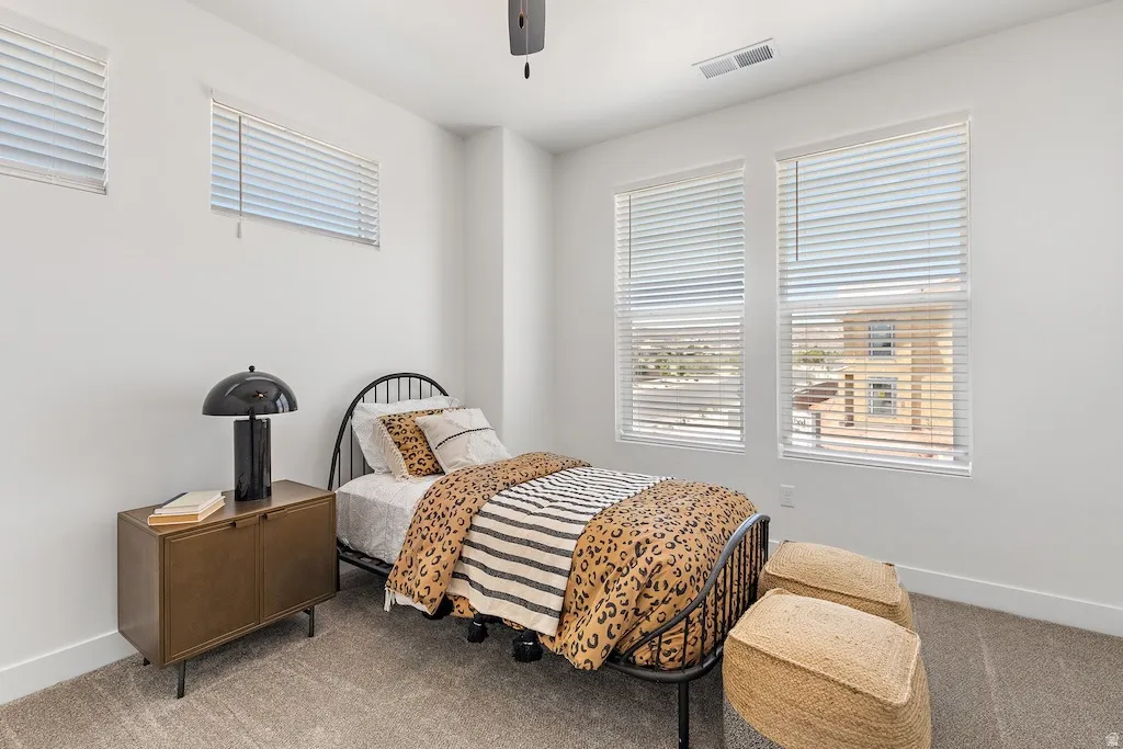 Bright room featuring white walls, textured carpeting, and a ceiling-mounted fan