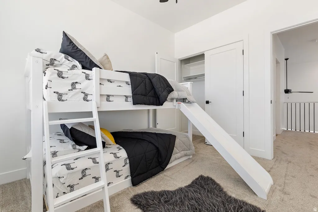 Bright interior room featuring a built-in bunk bed with ladder and slide, plush carpet flooring, and a closet with shelving
