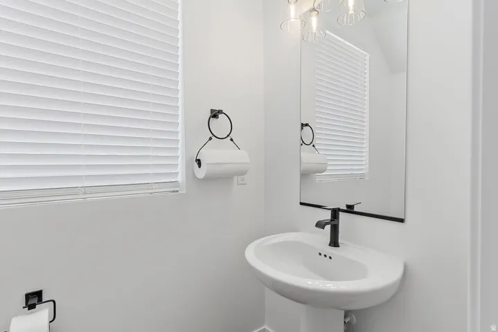 Pedestal sink with matte black faucet, wall-mounted rectangular mirror, and complementary overhead light fixture