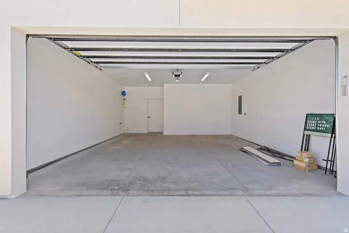 Spacious garage featuring concrete flooring, white painted walls, overhead fluorescent lighting, a built-in garage door opener, and a side access door