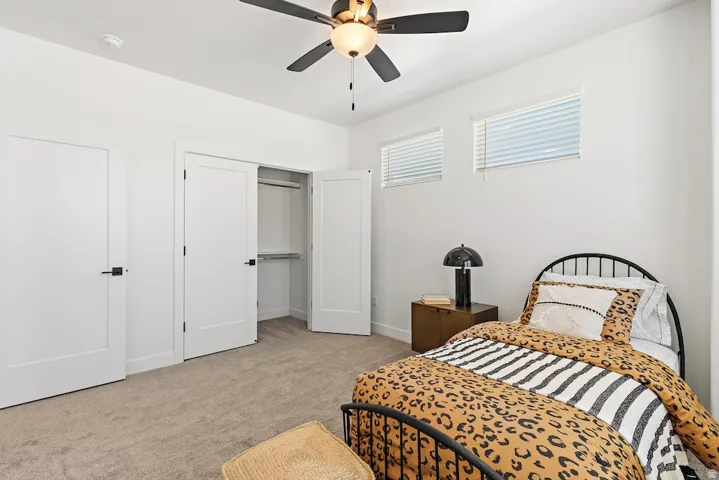 Spacious room featuring neutral carpet flooring, a ceiling fan with integrated lighting, two windows with blinds, and white doors with matte black hardware