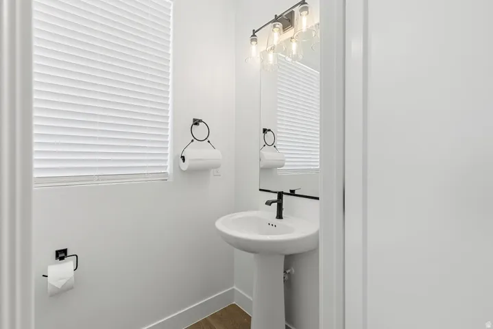 Pedestal sink with a matte black faucet, wall-mounted mirror, and industrial-style vanity lighting