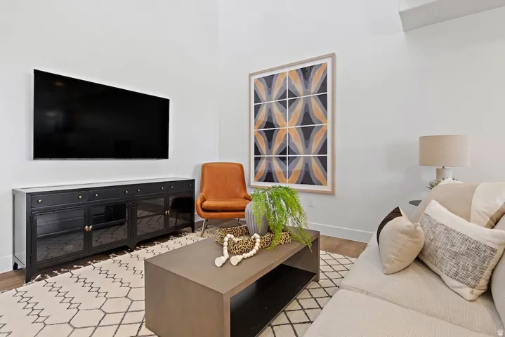Vaulted ceiling enhancing the spacious living area, featuring wood-finish flooring and a contemporary media console with glass-front cabinetry