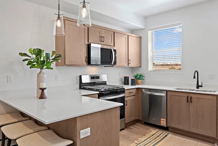 Kitchen featuring light wood-finish cabinetry, white countertops, stainless steel appliances, and two pendant lights