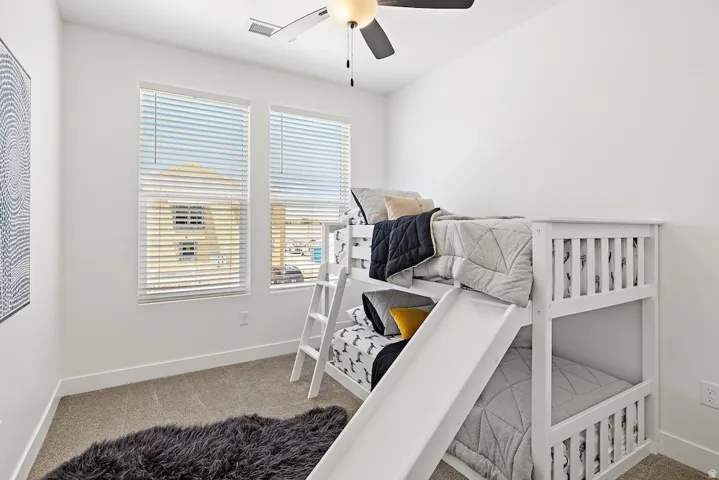 Bright room featuring two windows with blinds, neutral carpeting, and a ceiling fan with integrated lighting