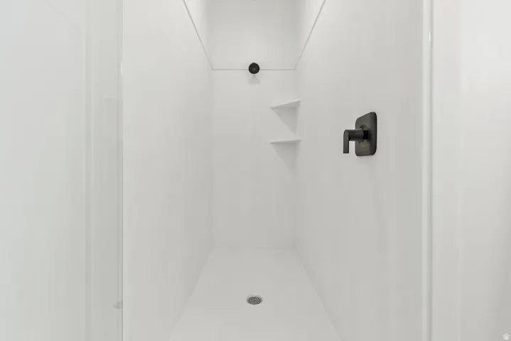 White shower enclosure with dark bronze fixtures, featuring a square shower head and integrated corner shelving