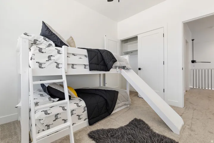 Bright interior room featuring a built-in bunk bed with ladder and slide, plush carpet flooring, and a closet with shelving