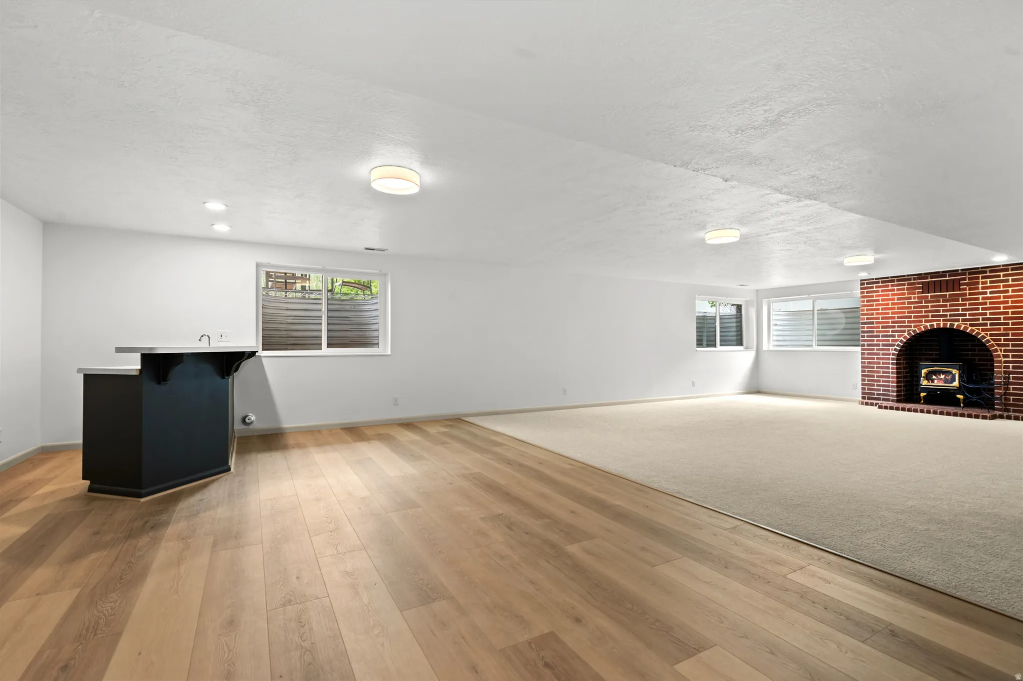 Lower-level recreation room featuring wood-finish flooring, a built-in wet bar with a solid surface countertop, and a brick fireplace with an insert