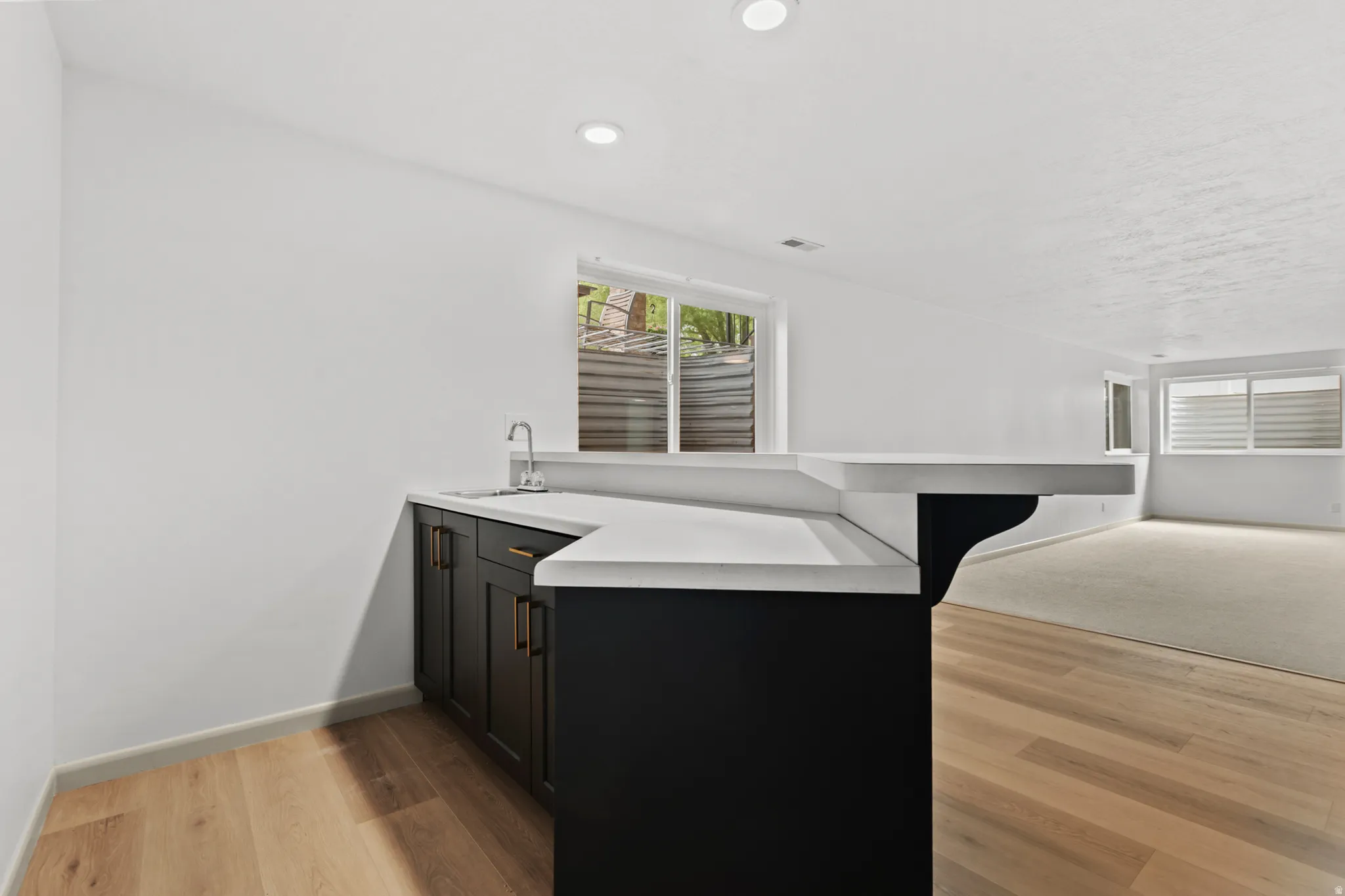 Wet bar featuring dark cabinetry, a countertop, and a stainless steel sink with a gooseneck faucet