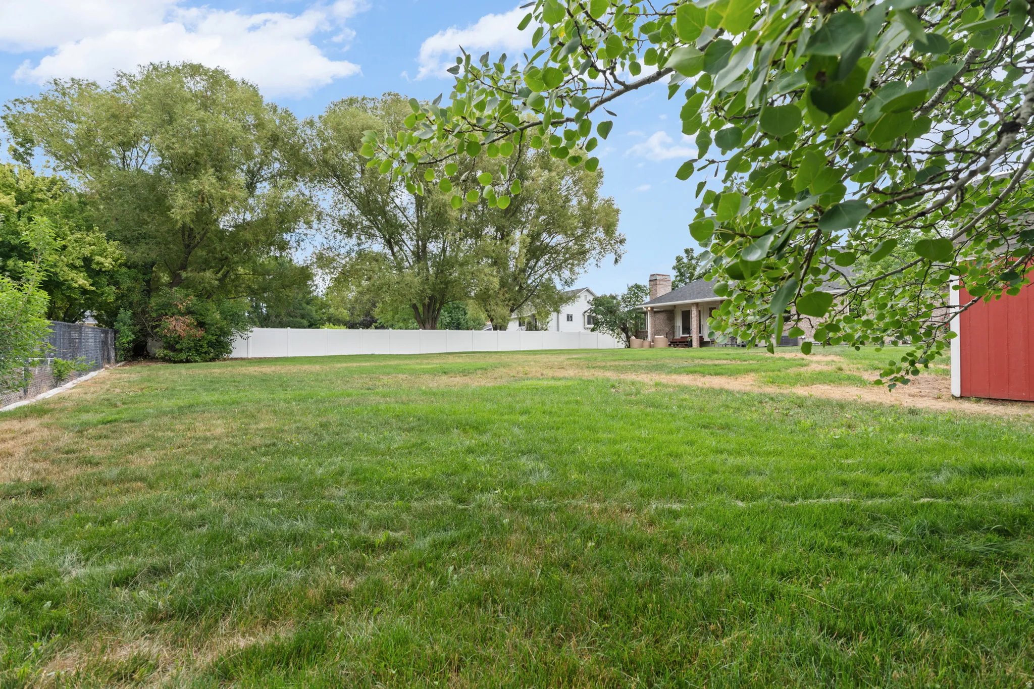 Expansive green lawn area featuring mature perimeter trees and a white privacy fence