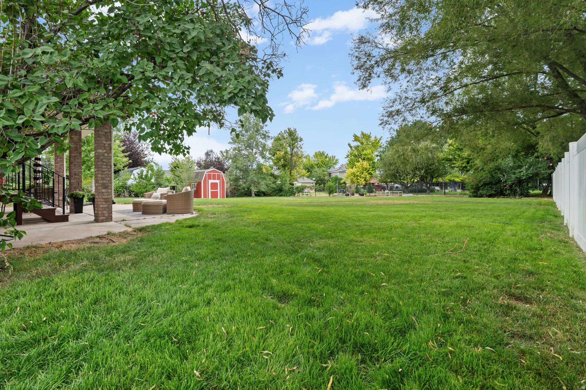 Expansive green lawn with mature trees and a detached red shed