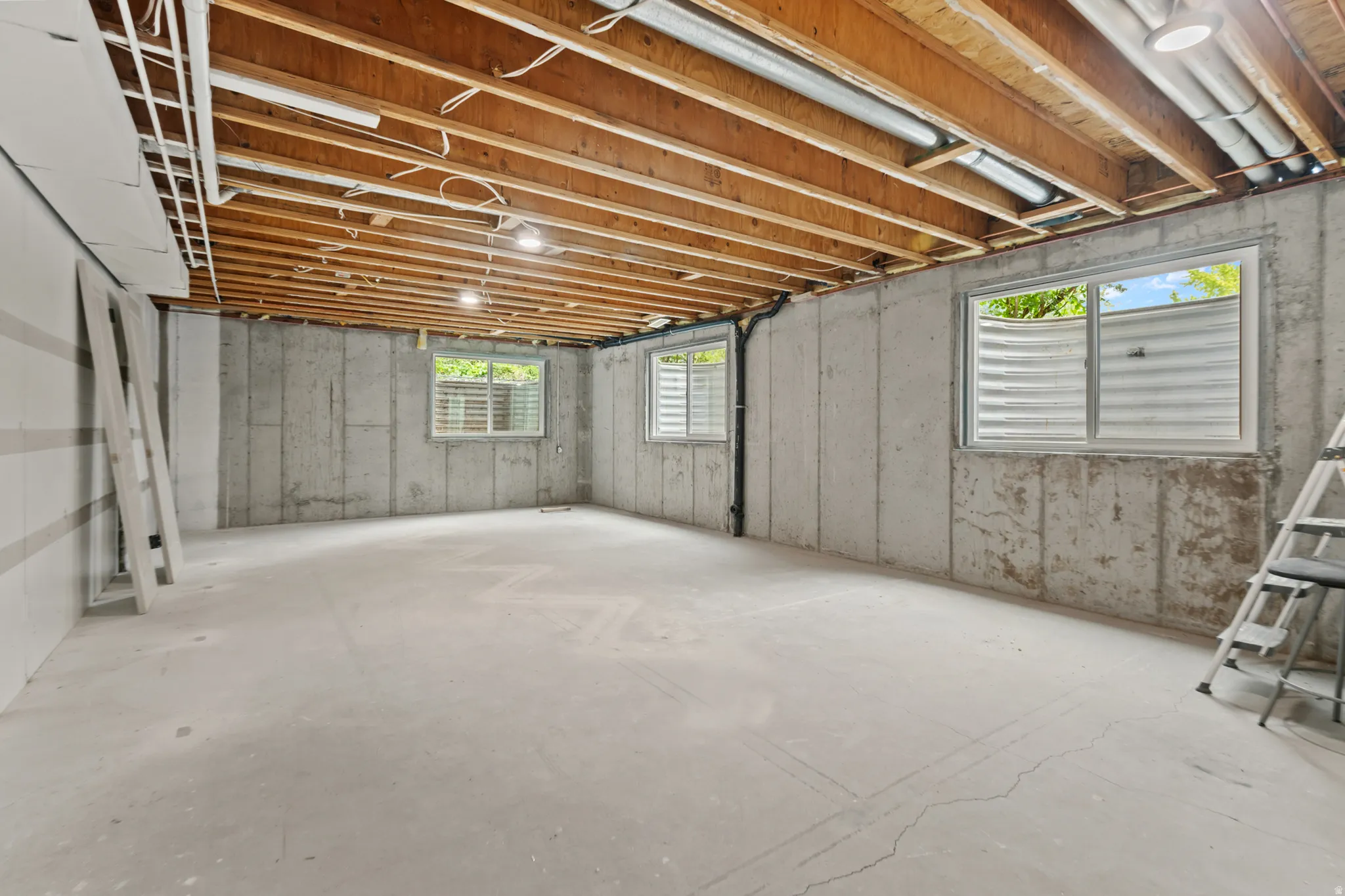 Unfinished basement with exposed wood joists, concrete walls, and concrete flooring