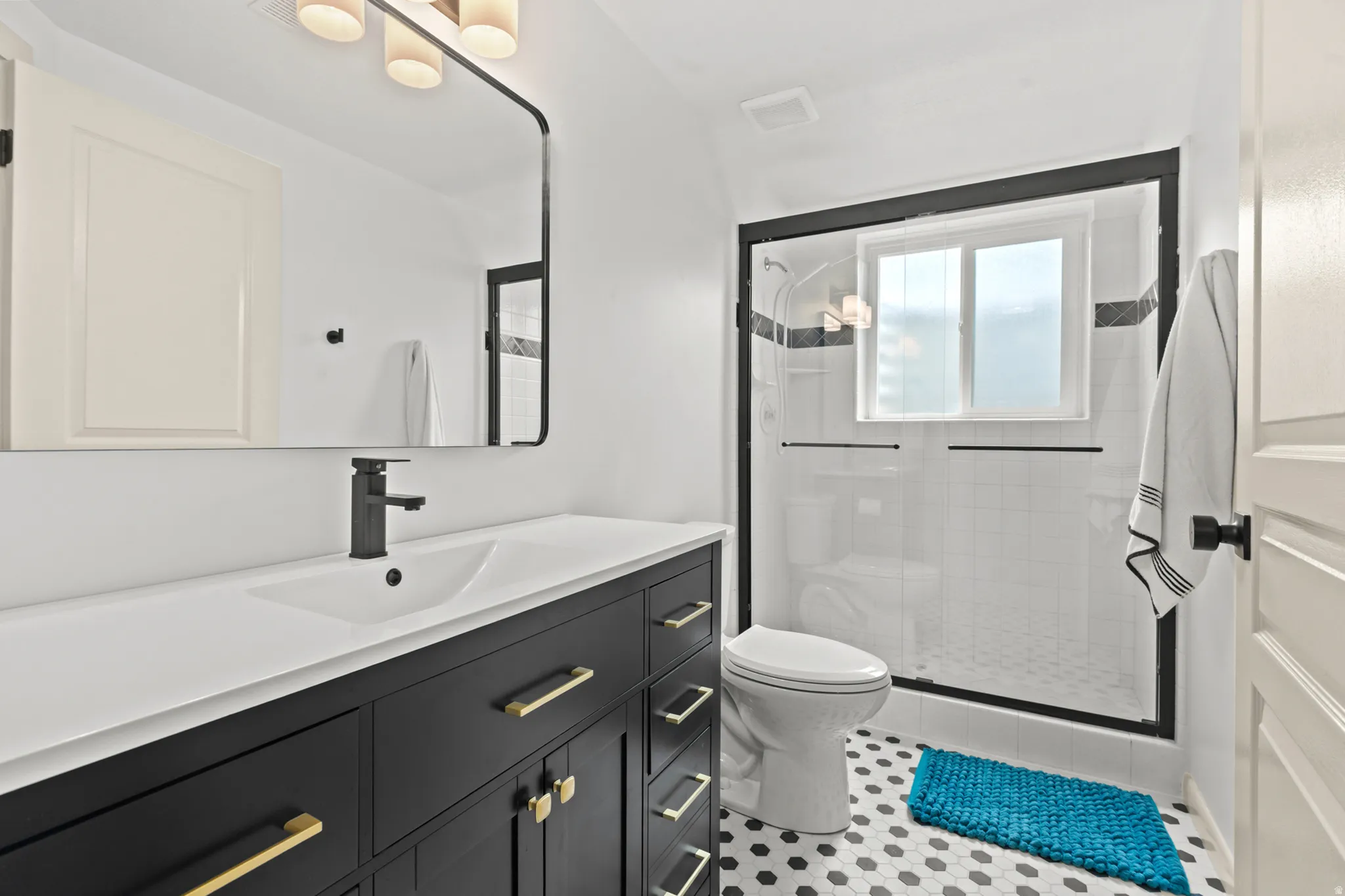 Bathroom featuring a dark wood-finish vanity with gold-tone hardware, a white integrated sink, a matte black faucet, and a large black-framed mirror