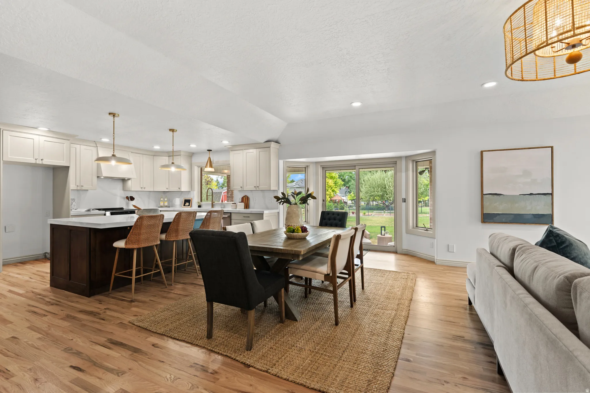 Open-concept living space featuring wood-finish flooring, a kitchen island with seating, white shaker cabinetry, a dining area, and sliding glass doors opening to the exterior