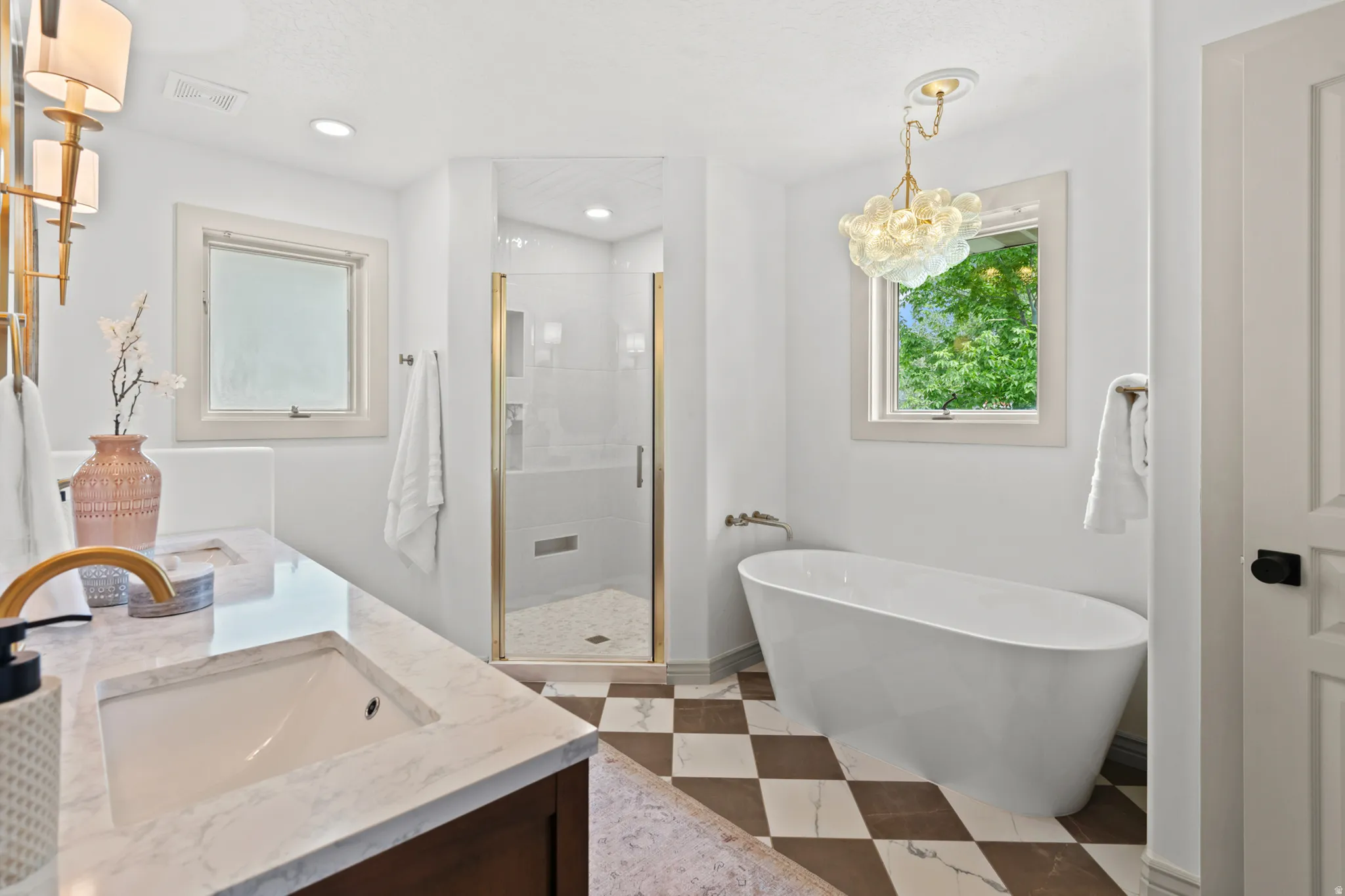 Spacious bathroom featuring a freestanding soaking tub, a glass-enclosed shower with gold-toned hardware, and a double vanity with a stone countertop