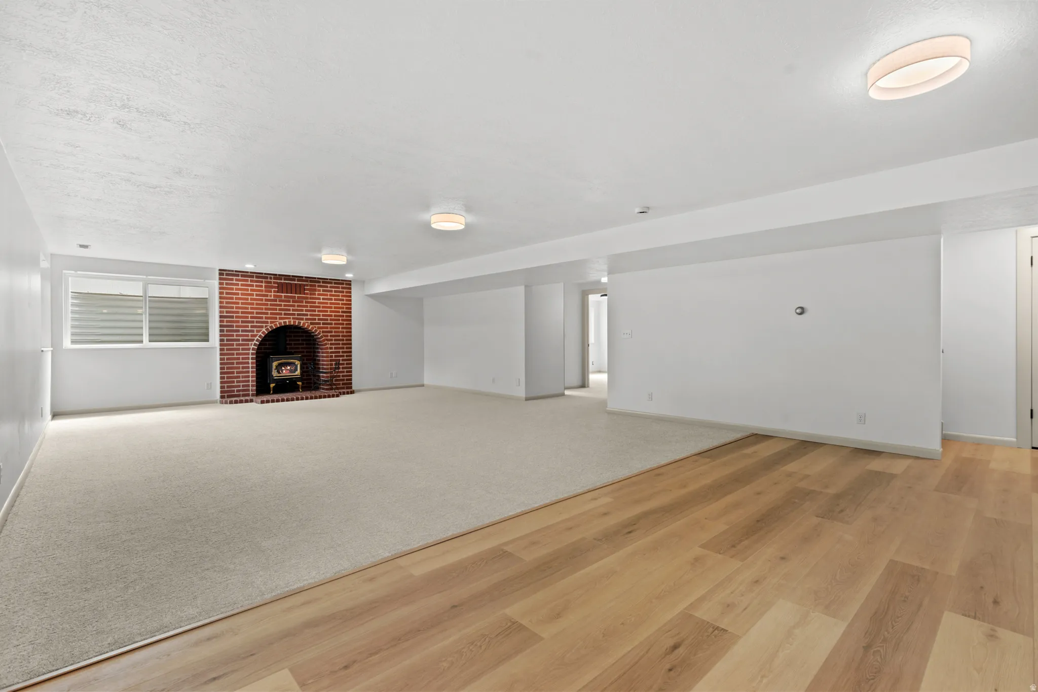 Spacious room featuring a brick fireplace with a wood-burning stove insert, wood-finish flooring, and light-colored carpeting