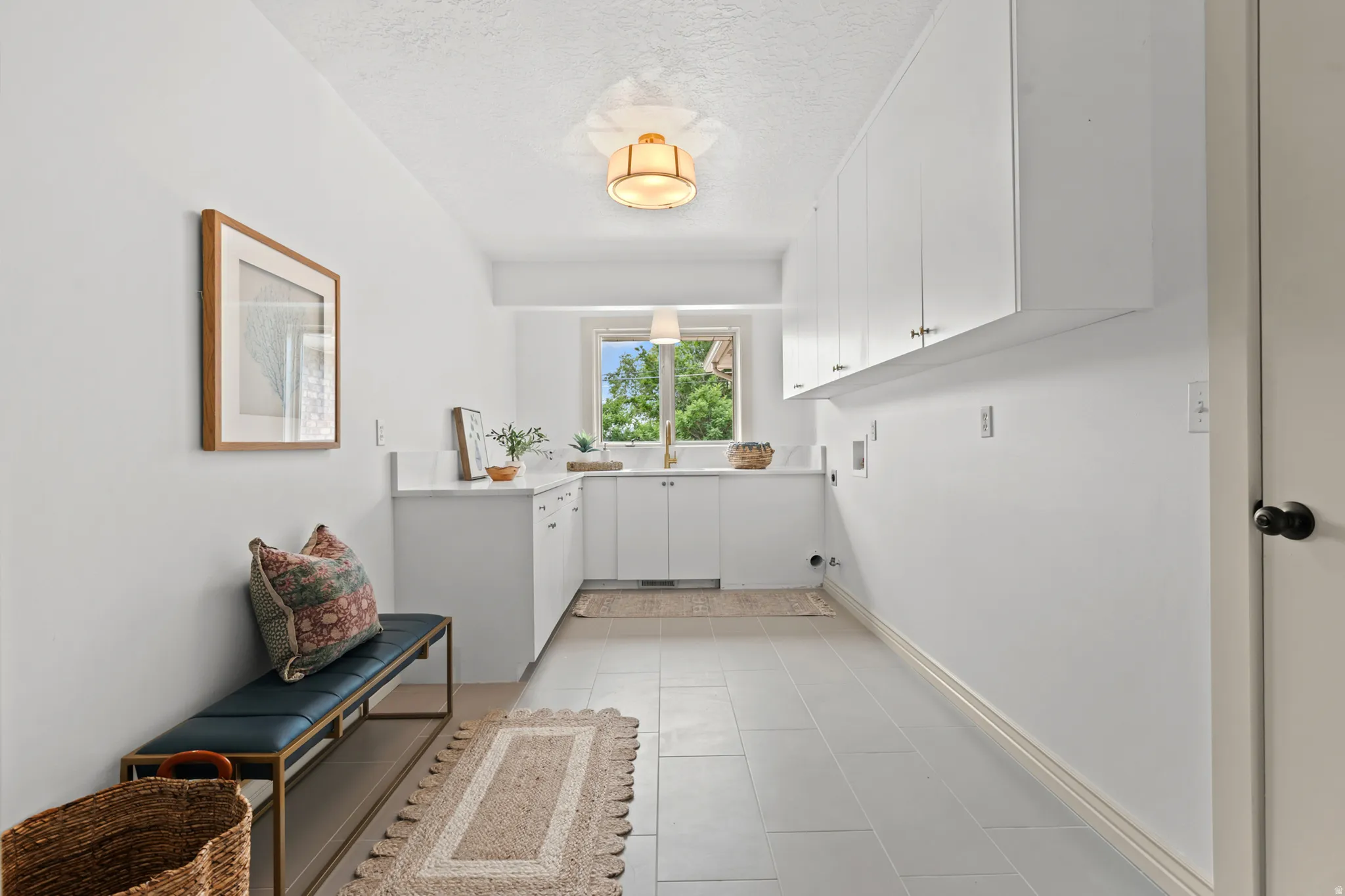 Utility room with a light tile floor, extensive white cabinetry, a sink with a gold-finish faucet, and a countertop space