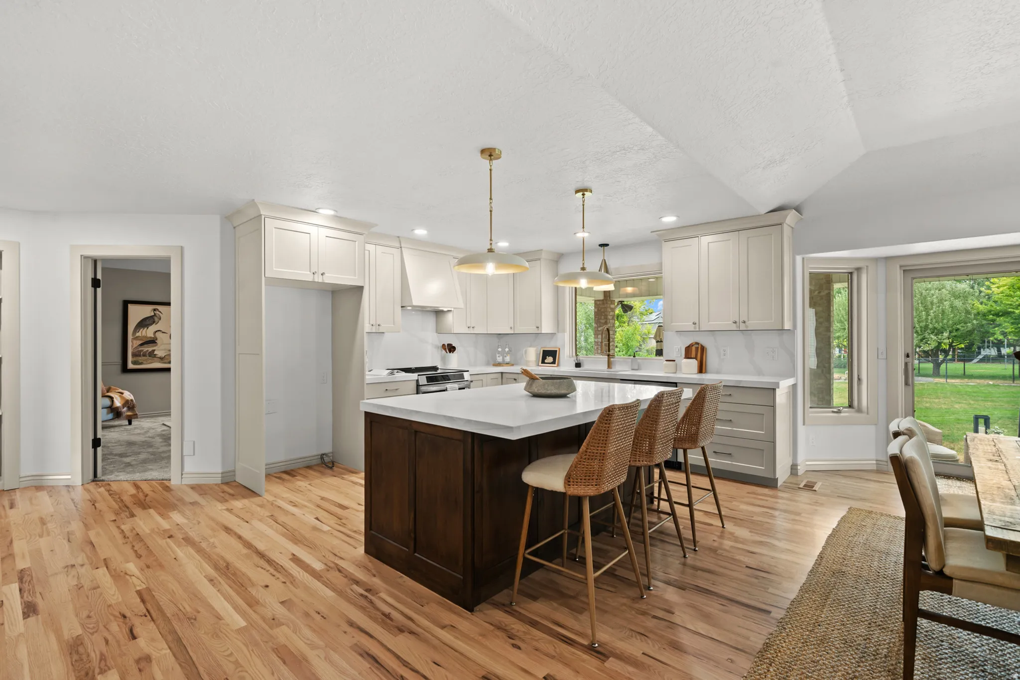 Kitchen featuring a large central island with a light-colored countertop, light wood-finish flooring, white upper cabinetry, and a white tile backsplash
