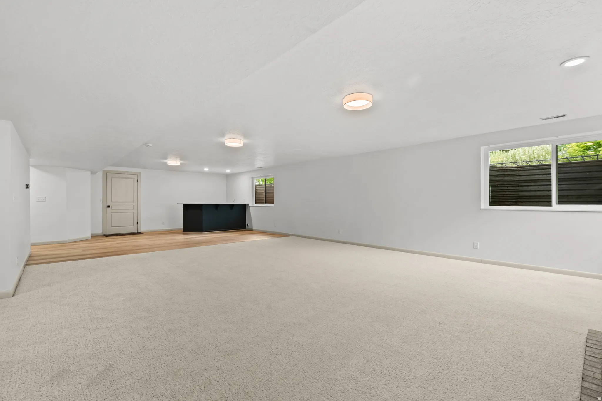 Spacious lower-level room featuring light-colored carpeting, recessed lighting, and a window providing natural illumination
