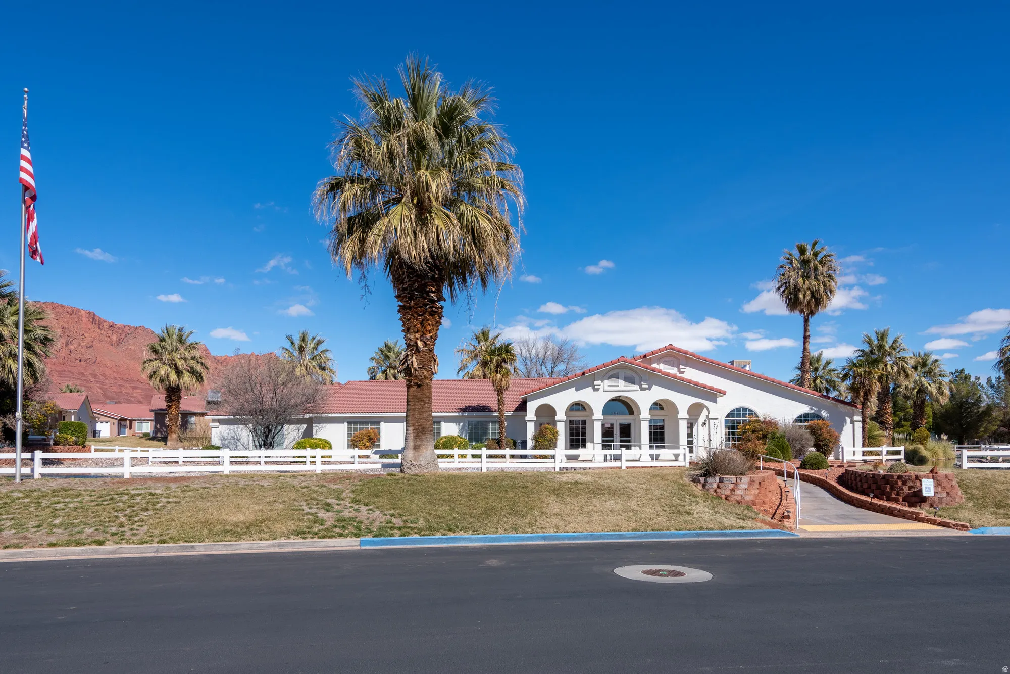 Single-story stucco exterior with a tiled roof, featuring arched windows and a white picket fence