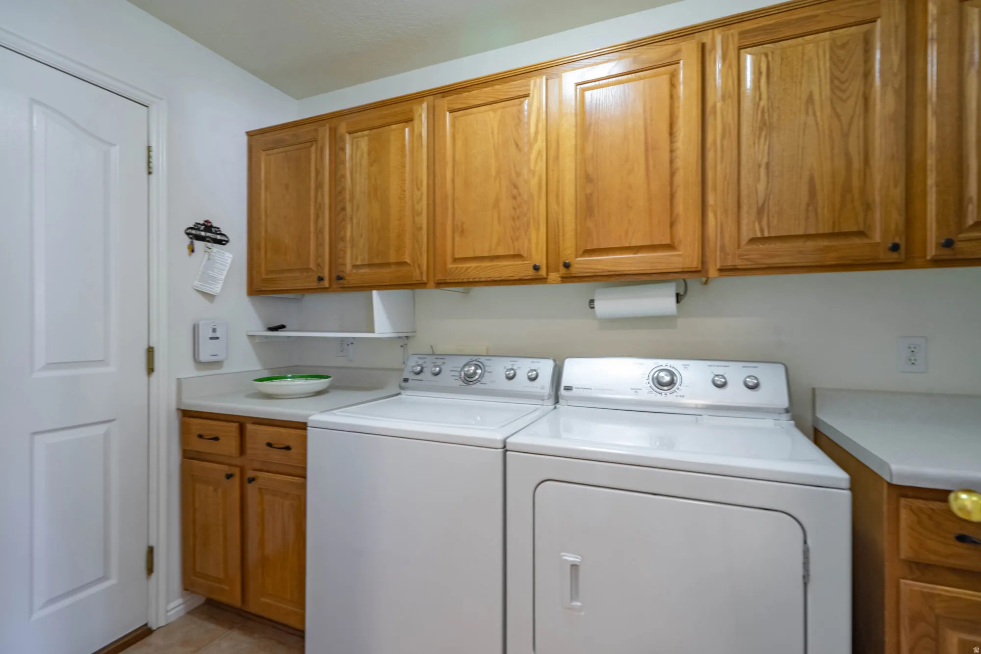 Laundry area featuring wood-finish cabinetry, white countertops, built-in shelving, and a paper towel dispenser