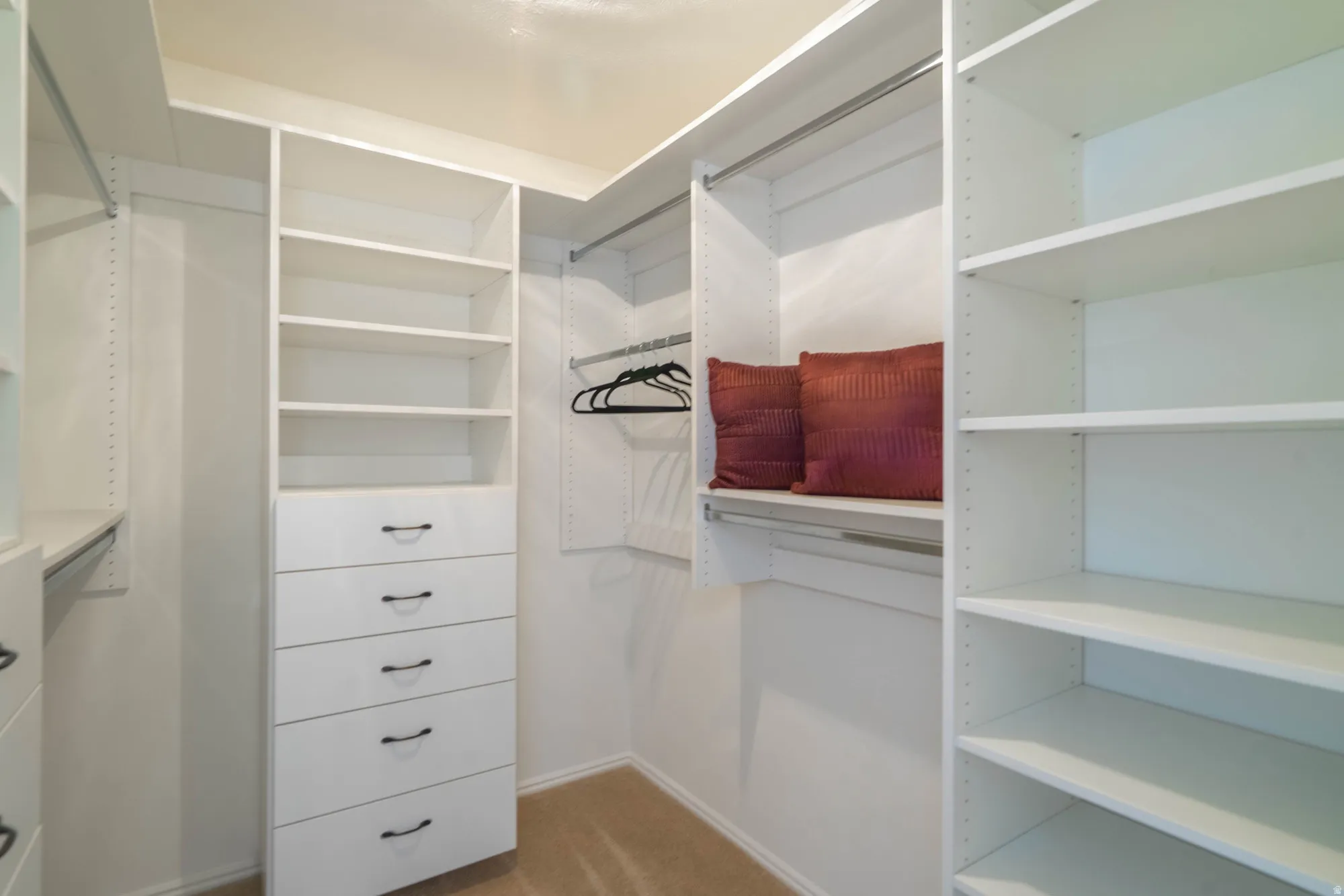 Walk-in closet featuring white built-in shelving, multiple hanging rods, and a five-drawer dresser unit with dark hardware