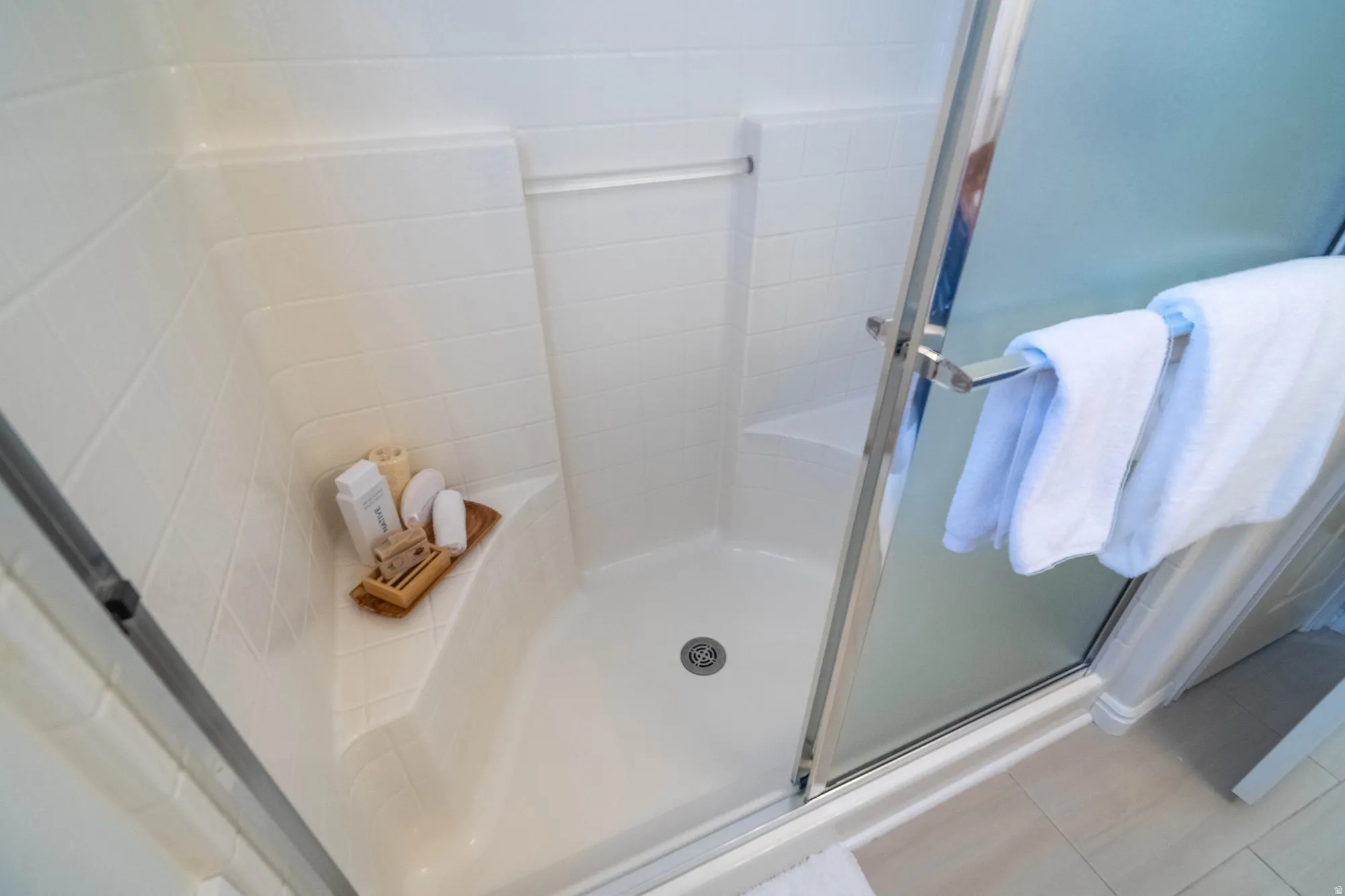 Shower enclosure with a built-in corner bench and integrated shelving