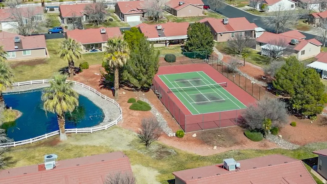 Community amenities featuring a tennis court, a pond with a white fence, and mature palm trees