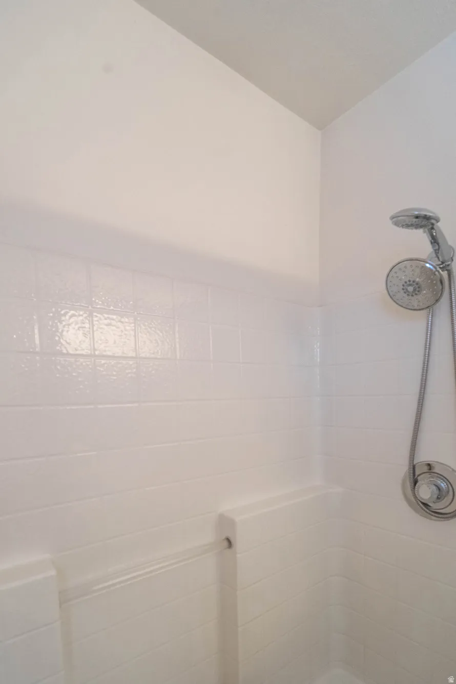 Shower stall featuring white subway tile, a chrome showerhead with a handheld sprayer, and an integrated corner shelf