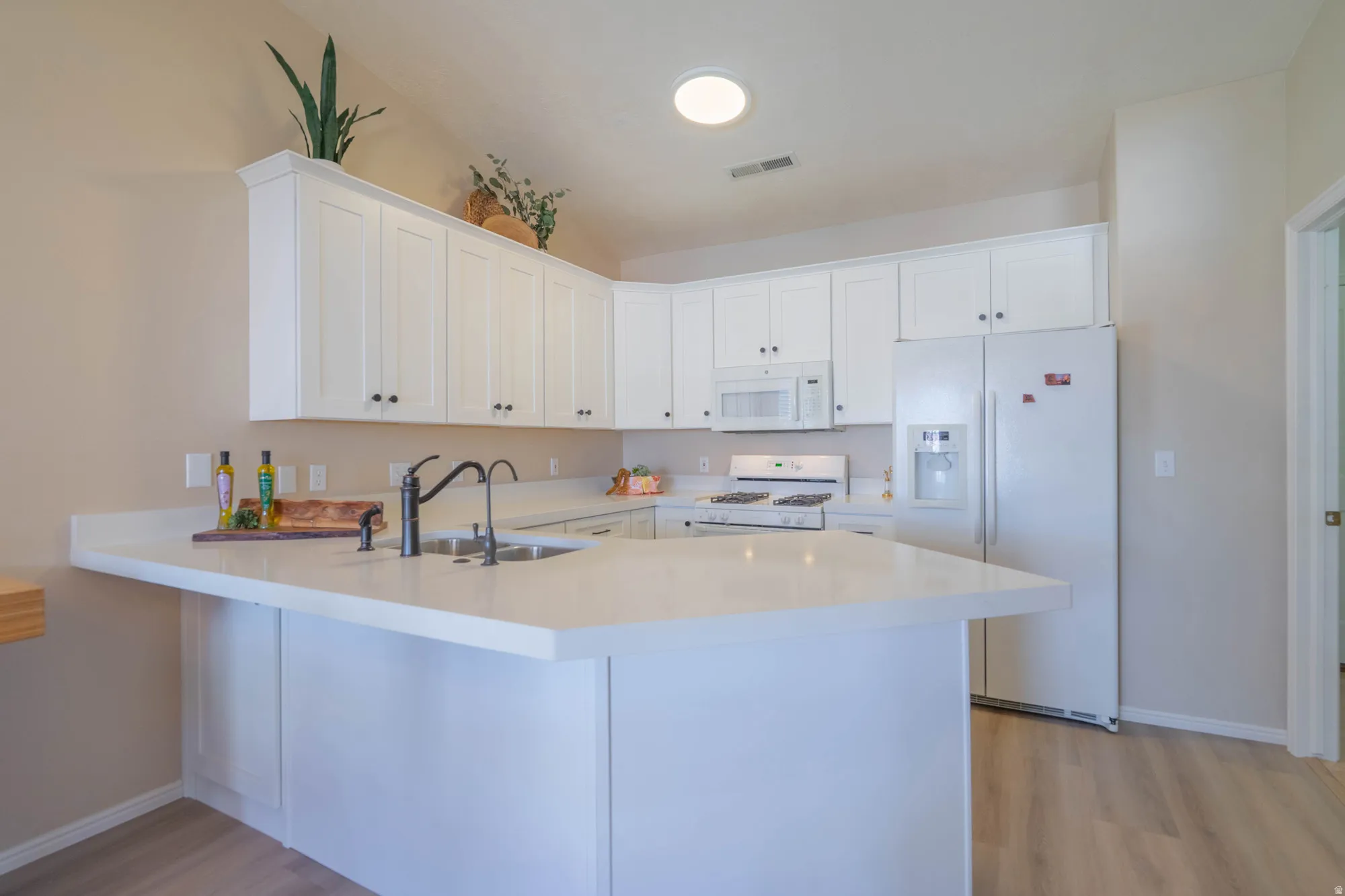 Contemporary kitchen featuring white cabinetry, light countertops, a stainless steel sink with a matte black faucet, and wood-finish flooring