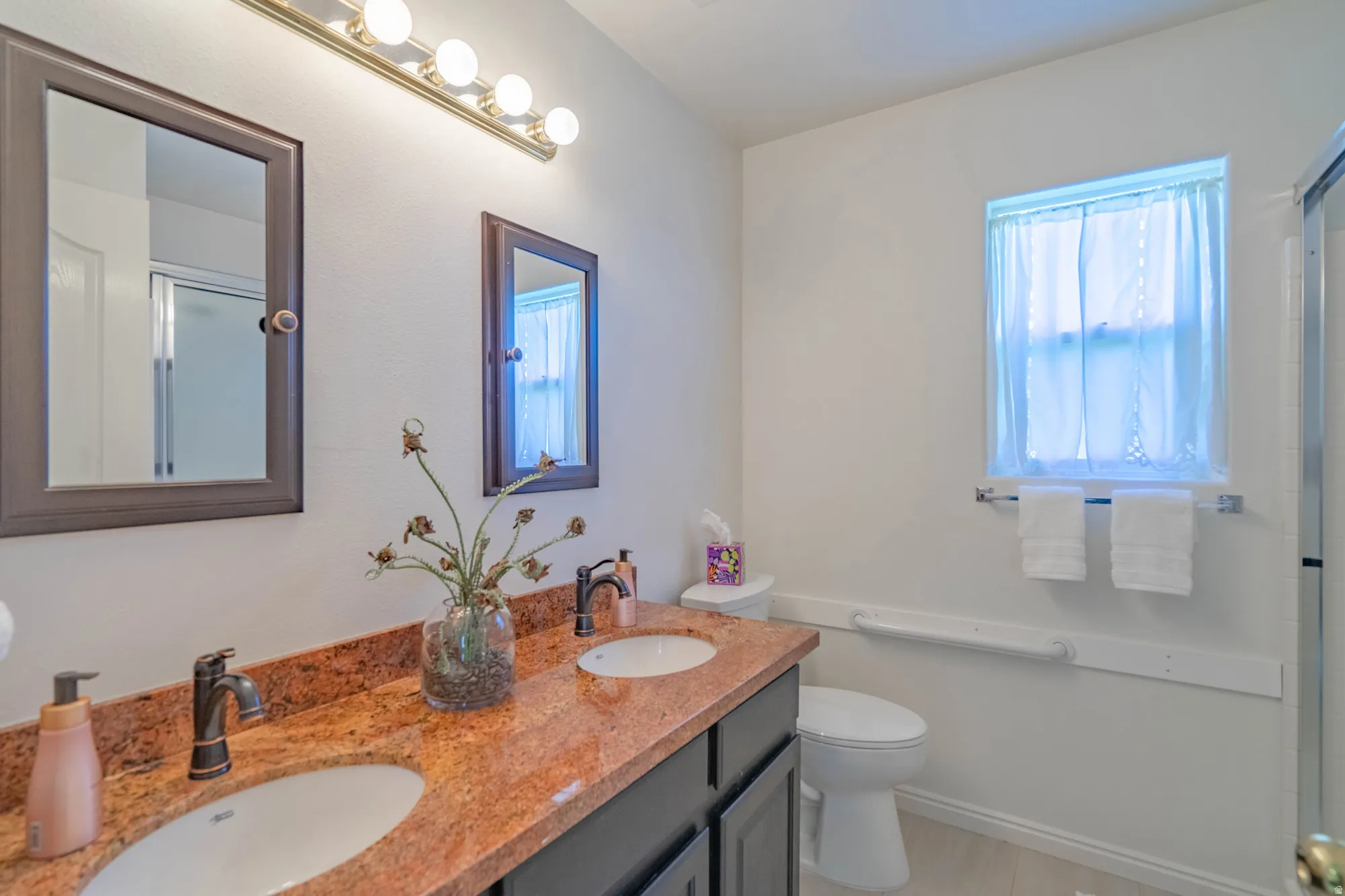Dual vanity with a stone countertop, individual framed mirrors, and dedicated lighting