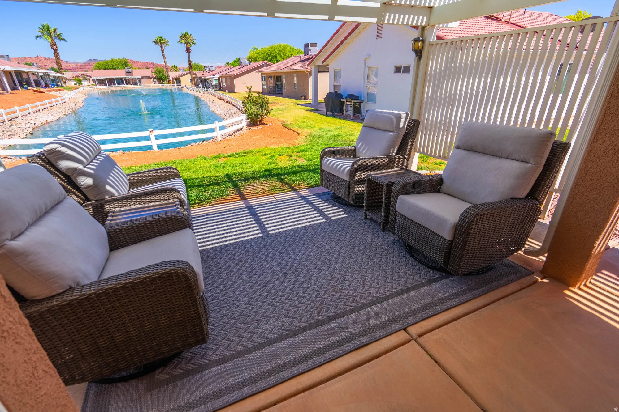 Covered patio with slatted pergola, overlooking a tranquil pond with a fountain feature