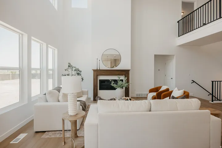 Two-story living area featuring a fireplace with a wood mantel, multiple large windows, and an open loft area with a black metal railing