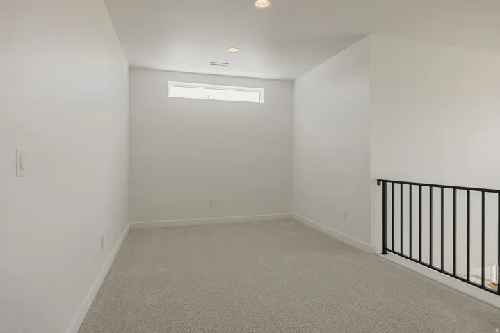 Carpeted secondary room featuring a horizontal accent window, white walls, recessed lighting, and a black iron railing