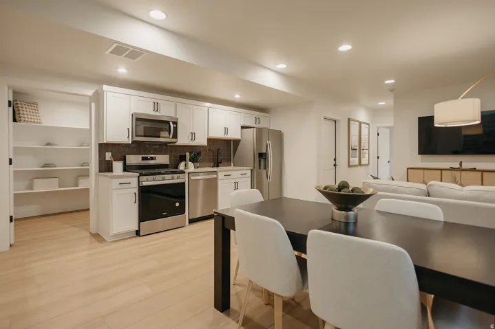 Modern kitchen featuring white cabinetry, stainless steel appliances, and a dark stone-finish backsplash