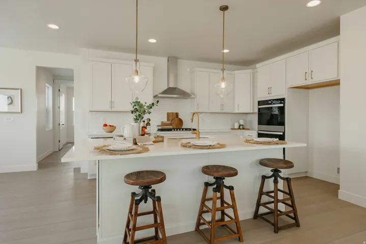 Kitchen featuring a central island with countertop seating, white cabinetry, a built-in double oven, a stainless steel range hood, and light wood-finish flooring