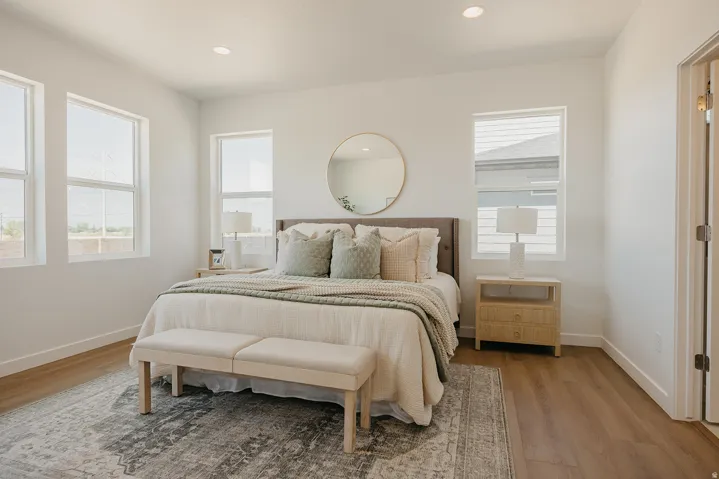 Spacious bedroom featuring wood-finish flooring, ample natural light from multiple windows, recessed lighting, and a neutral color palette