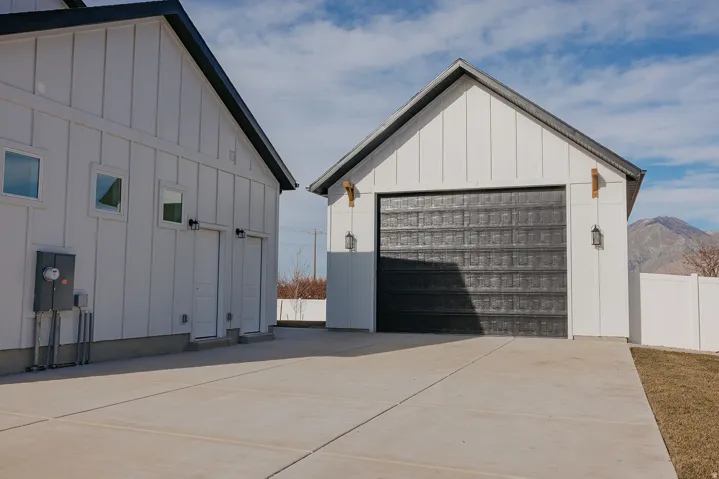 Detached garage with a dark textured door, board and batten siding, and exterior sconce lighting