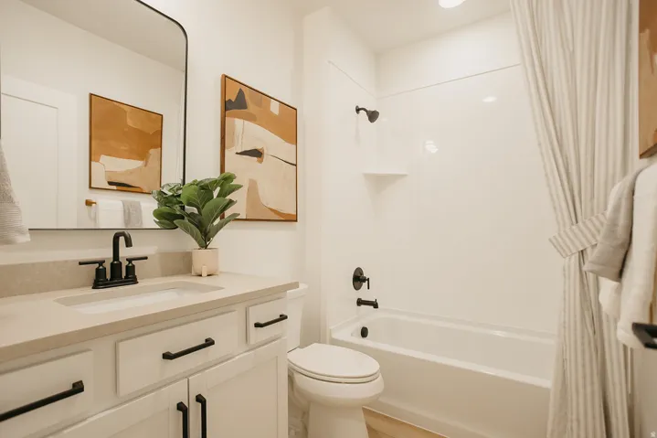 Contemporary bathroom featuring a white vanity with black hardware, a light-colored countertop with an integrated sink, a matte black faucet, and a white tub/shower combination