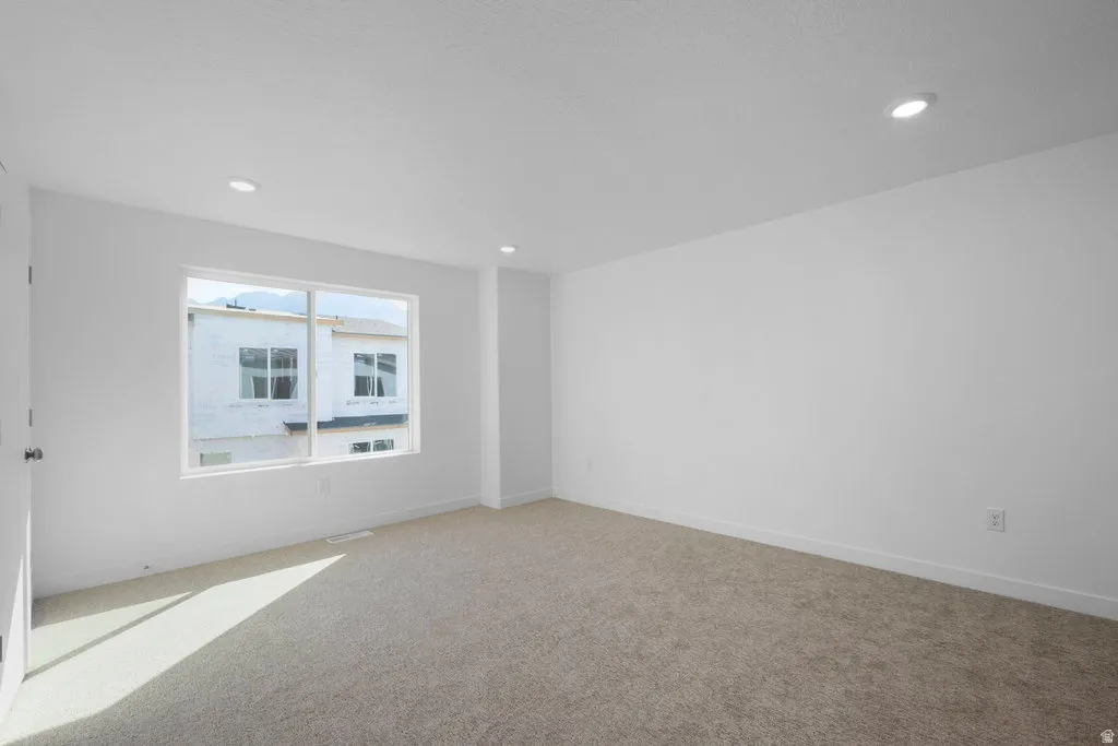 Spacious room featuring neutral carpeting, white painted walls, and recessed ceiling lighting