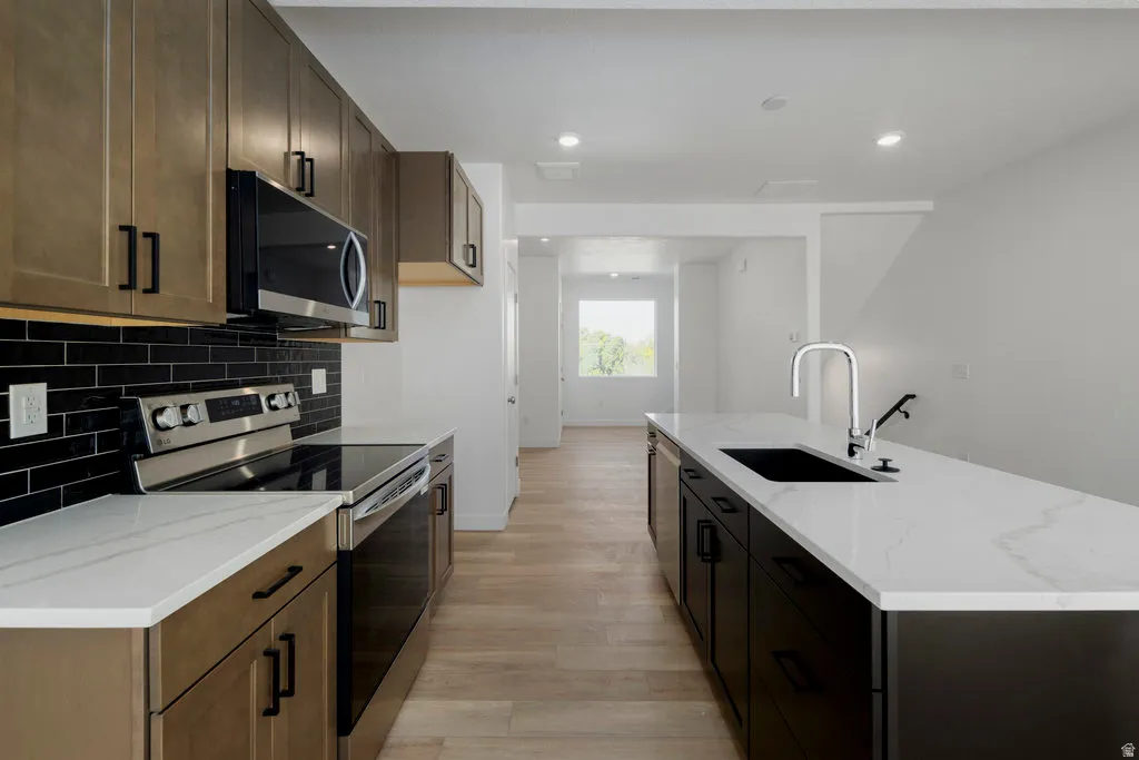 Modern kitchen featuring a large island with an undermount sink, white countertops, stainless steel appliances, dark wood-finish cabinetry, and a black subway tile backsplash