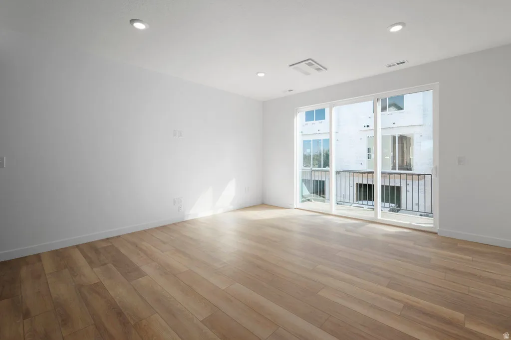 Expansive room featuring wood-finish flooring and a full-wall sliding glass door leading to a balcony with black metal railing