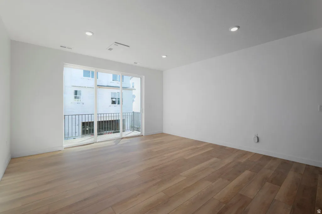 Spacious interior featuring wood-finish flooring, recessed lighting, and a sliding glass door opening to a private balcony with metal railings