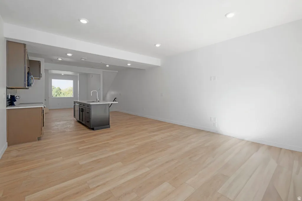 Open-concept living area featuring light wood-finish flooring, recessed lighting, and a modern kitchen island with an integrated sink
